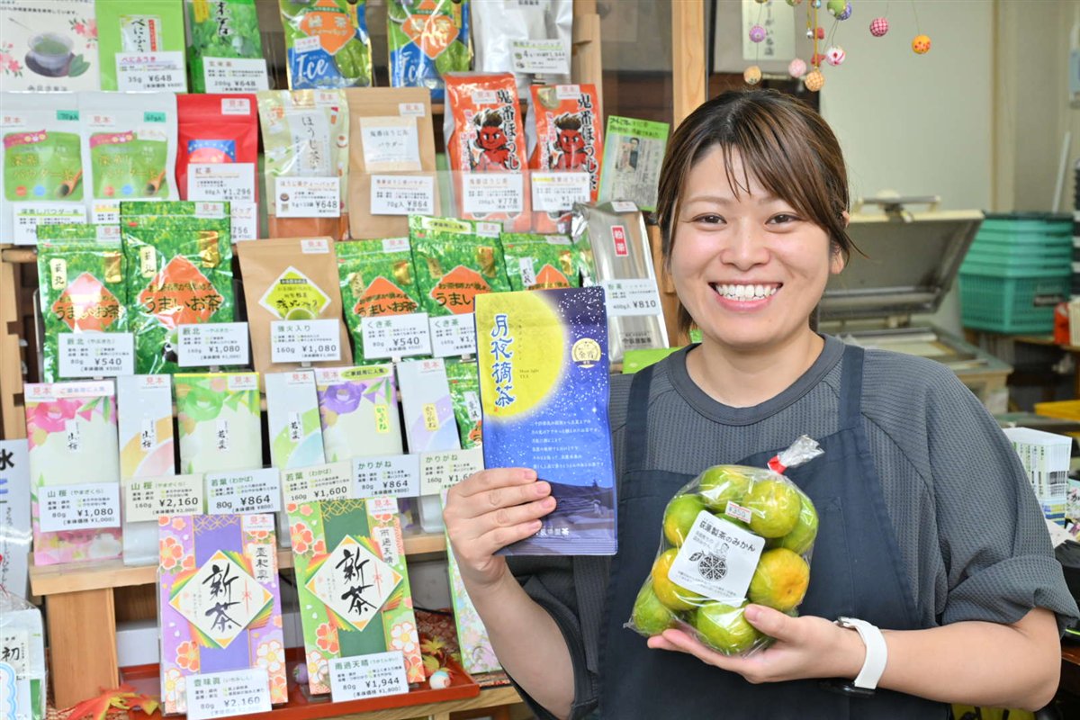 お茶の商品が並ぶ棚の前で、商品とみかんを持って笑うお店の方