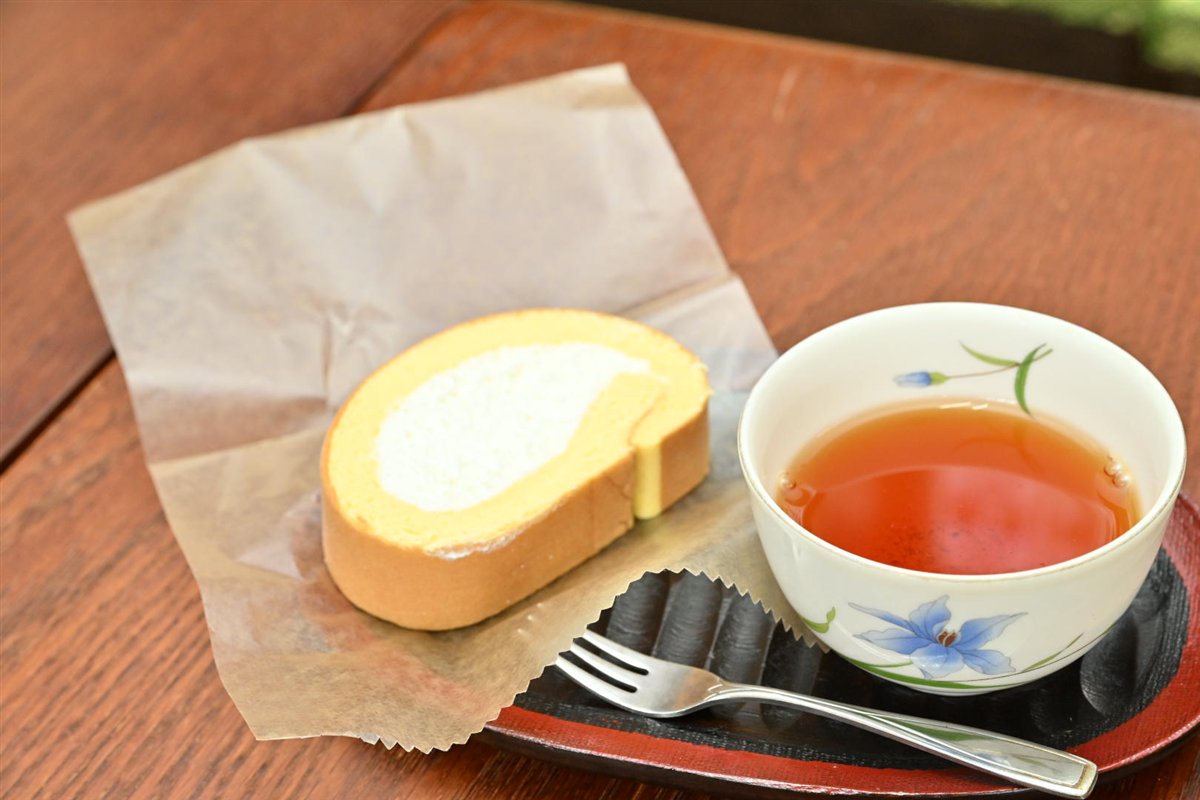 ロールケーキと紅茶を、木のテーブルの上で撮った写真